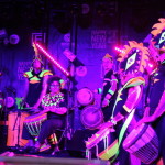 Dancer in bright costume with hair flying, drummers in back ground