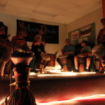 People sitting on a stage playing djembes